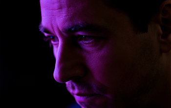 Potret close-up wajah trader dengan pencahayaan ungu setengah bayangan, menampilkan kelelahan sekaligus tekad bangkit.